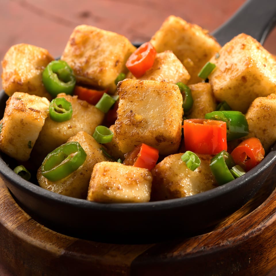 Close-up of golden fried paneer cubes with green and red chili peppers in a black pan.